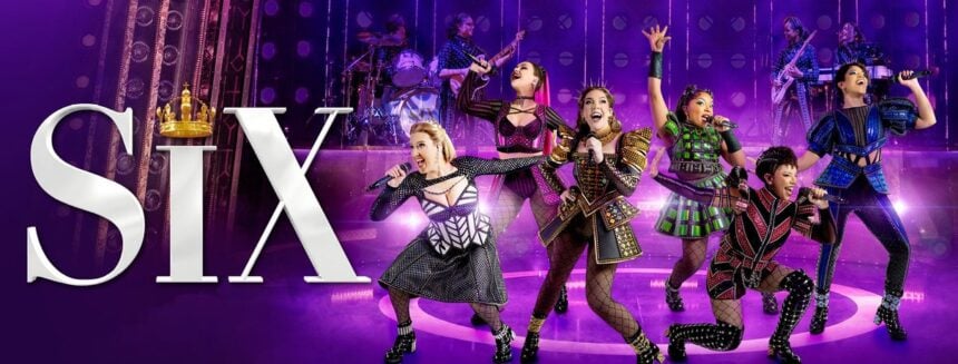 Six performers in colourful costumes sing and dance on a purple-lit stage in SIX The Musical at the Vaudeville Theatre London