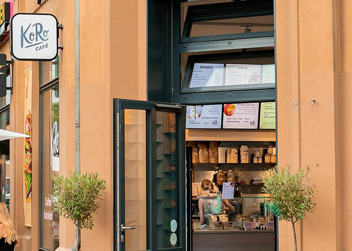 Frau vor dem KoRo Café in Berlin mit dem Café-Schild im Hintergrund