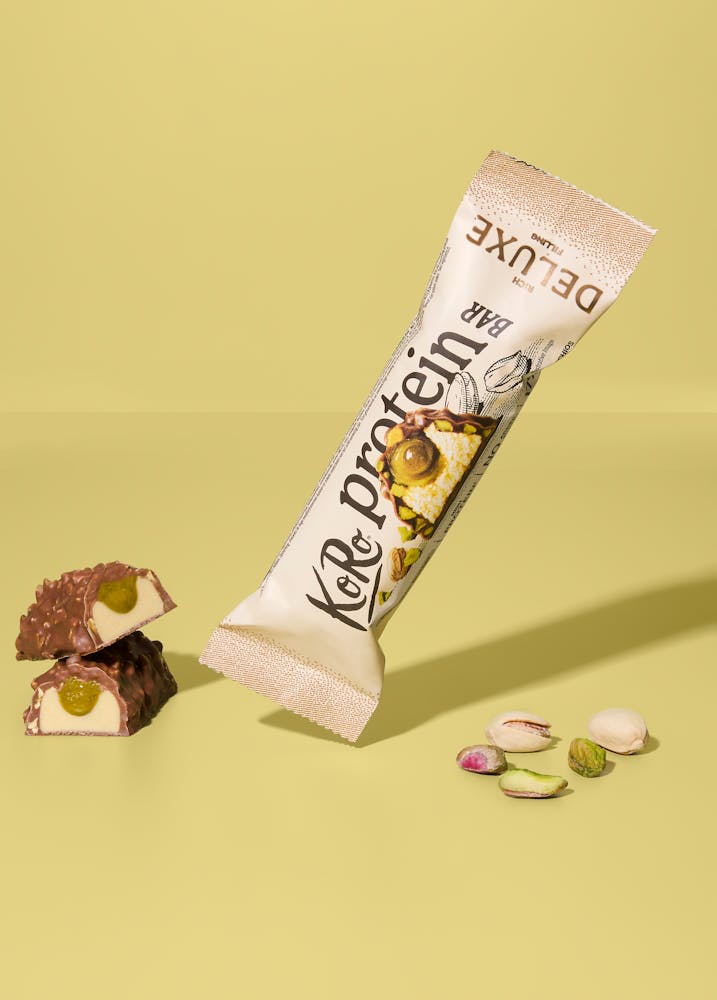 KoRo Protein Bar Deluxe mit Pistazienmus auf hellem gelbem Hintergrund