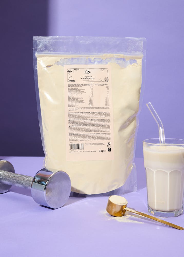 Tüte veganes Proteinpulver Vanille neben Glas und Hantel