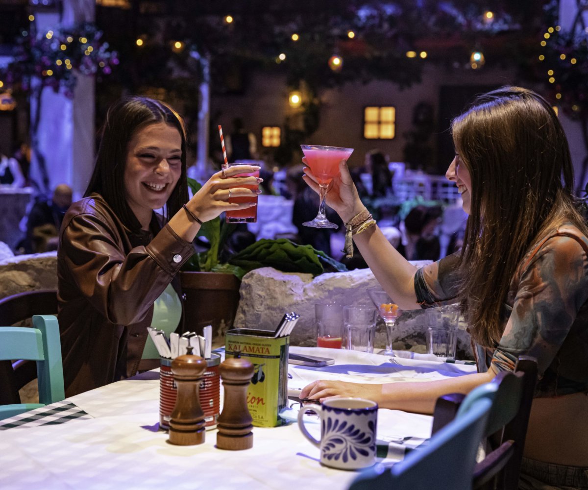 Two friends toasting cocktails at a table at Mamma Mia! The Party