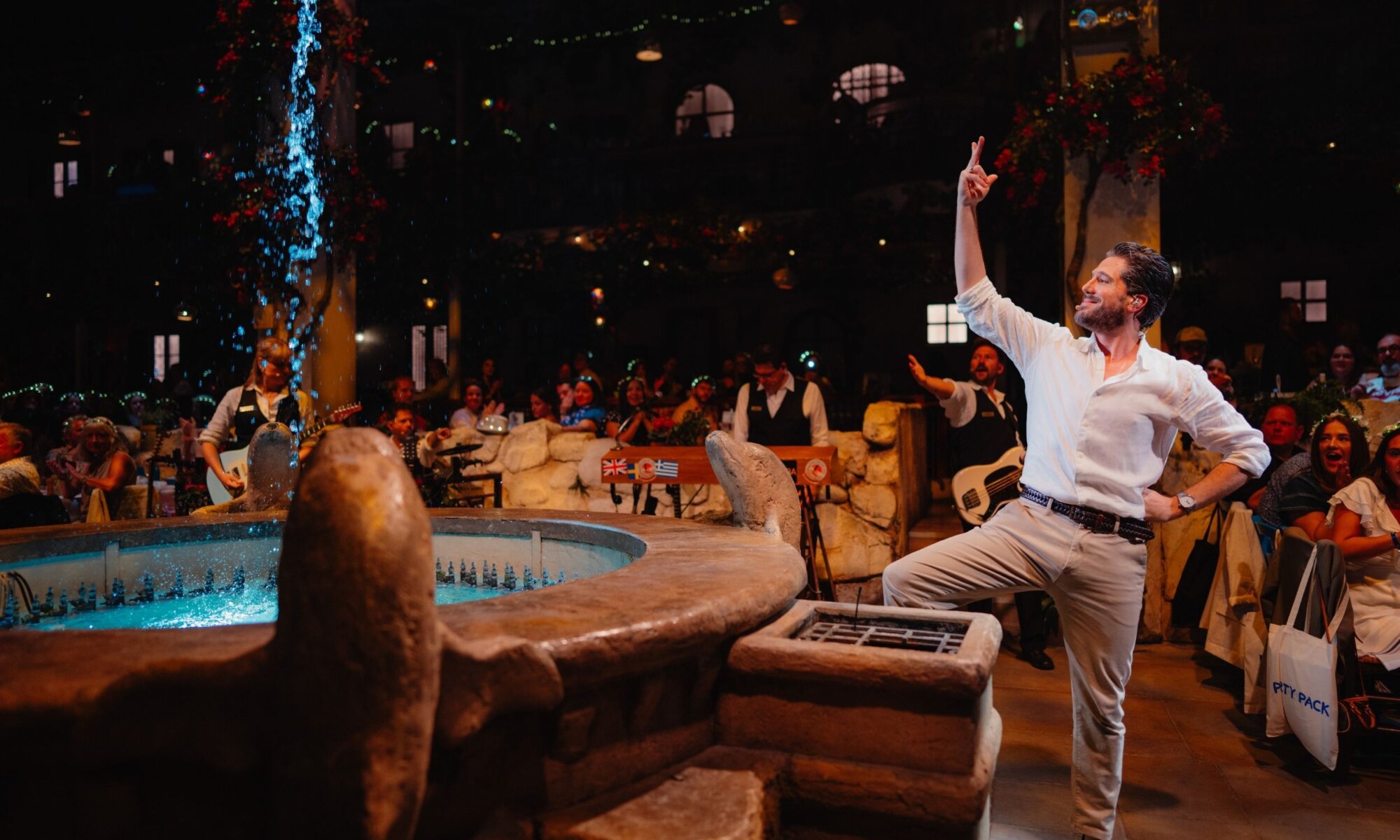 Male performer singing beside the taverna fountain with the live band behind