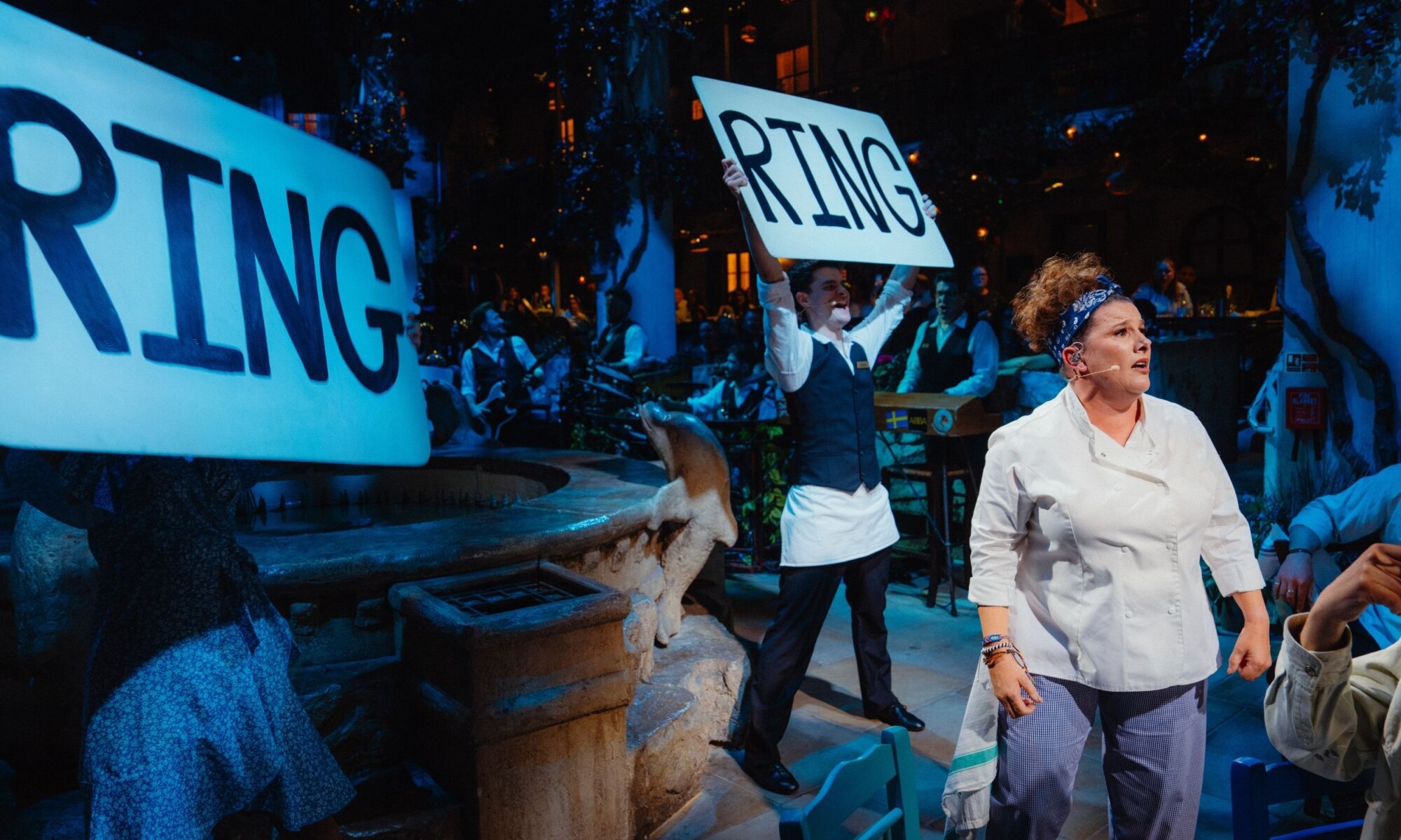Cast performing a live scene with the band during Mamma Mia! The Party
