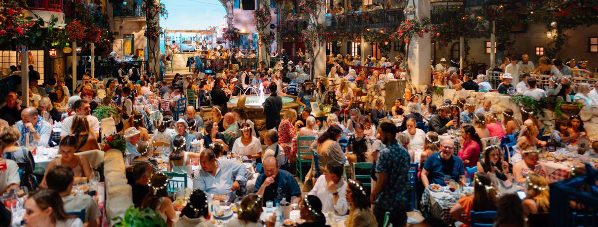 Packed Nikos taverna set with guests in flower crowns at Mamma Mia! The Party