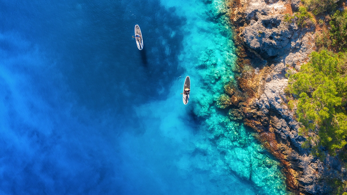 Two people paddling kayaks near a coast