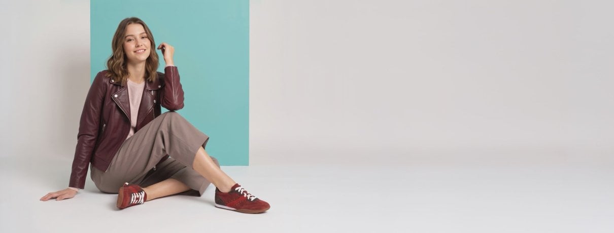Model seated in autumn clothing wearing burgundy Aetrex sneakers