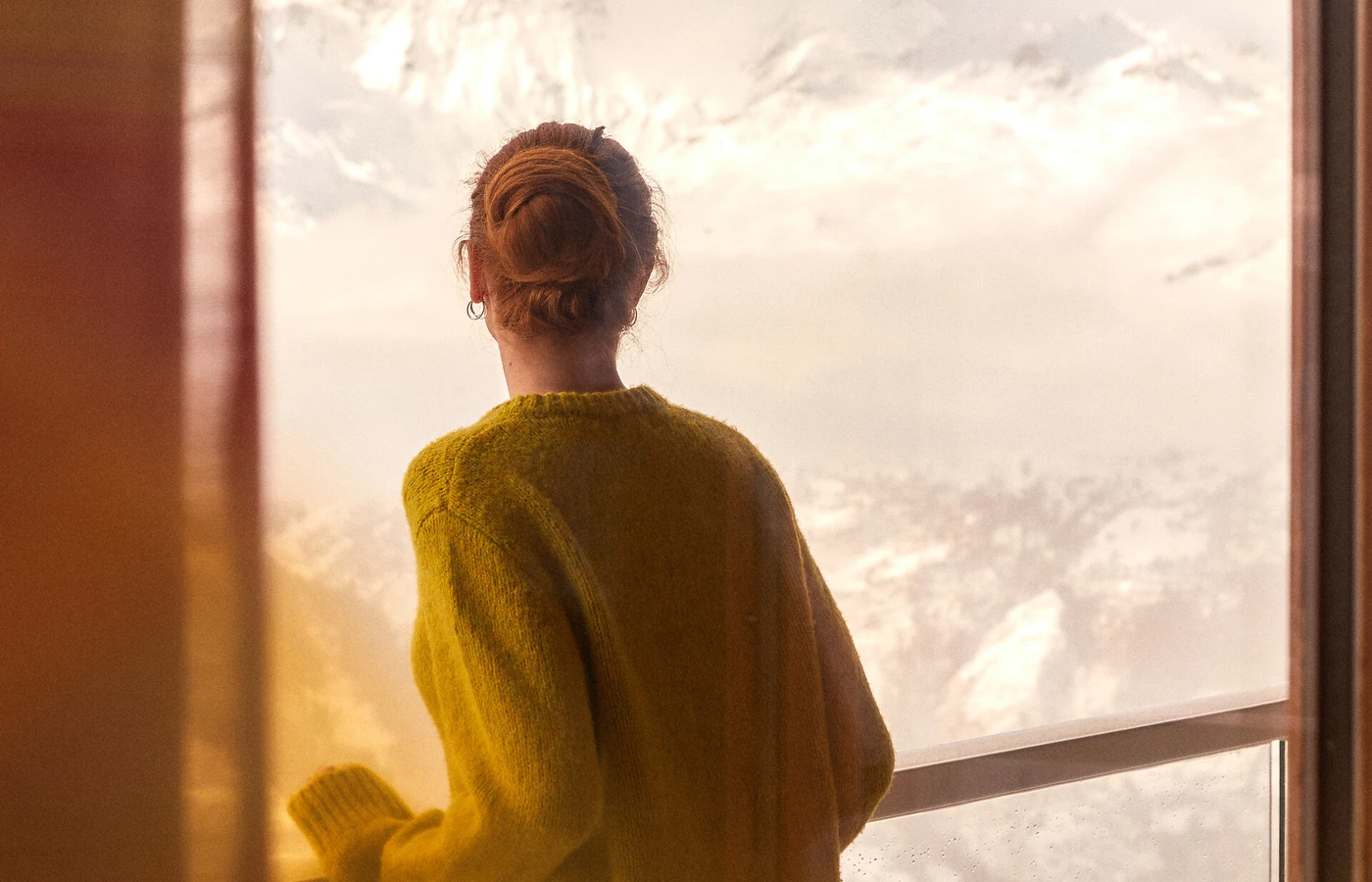 Woman looking toward a snowy mountain through a resort window