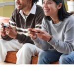 Zwei Menschen spielen gemeinsam auf einer Konsole auf dem Sofa