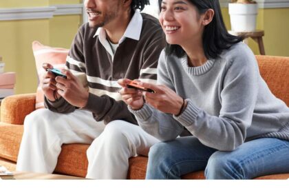 Zwei Menschen spielen gemeinsam auf einer Konsole auf dem Sofa