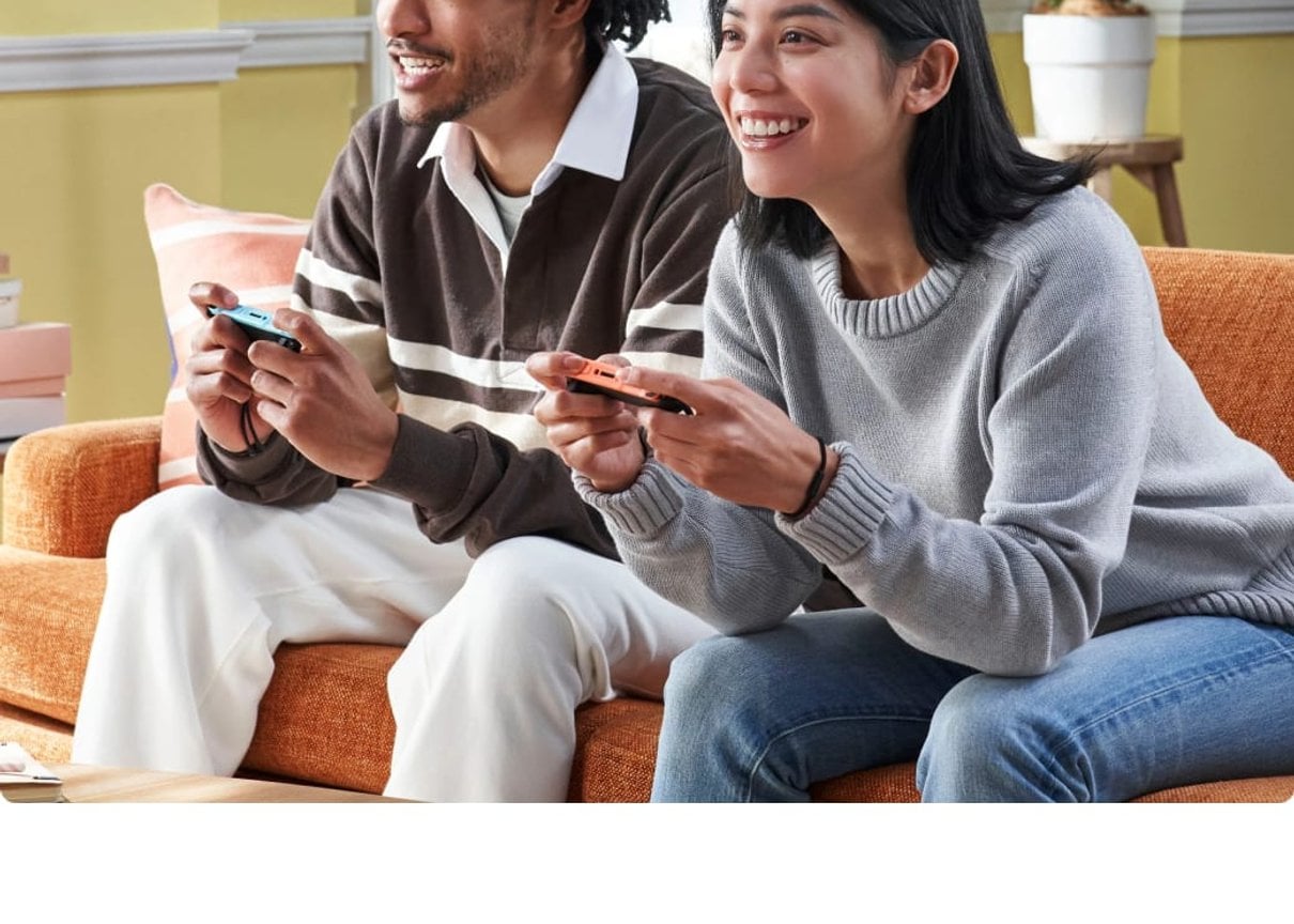 Zwei Menschen spielen gemeinsam auf einer Konsole auf dem Sofa