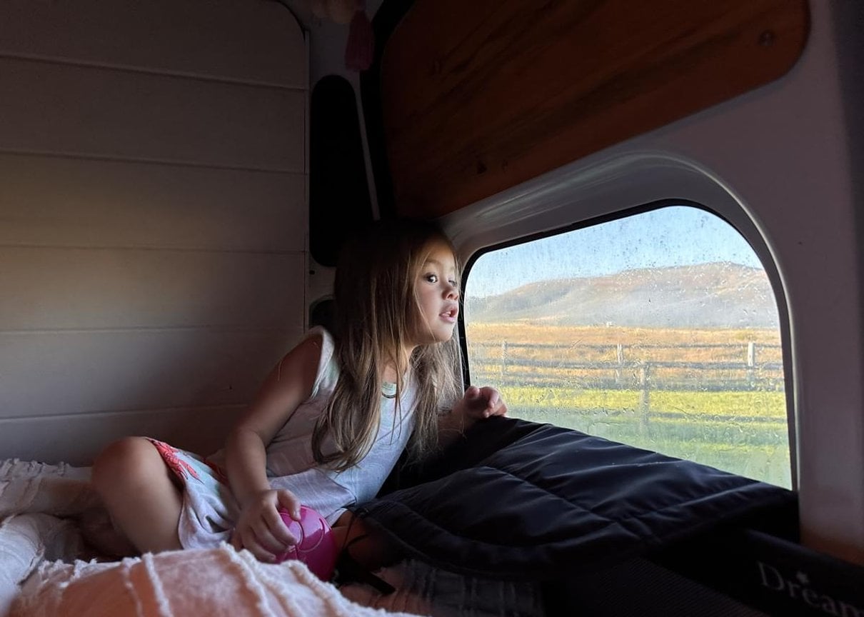 Child looking out from inside a camper at a Harvest Hosts location