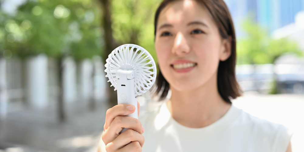 Frau hält bei sommerlicher Hitze einen Handventilator