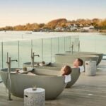Guest relaxing beside an outdoor spa pool with autumn trees behind