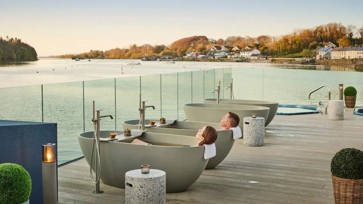 Guest relaxing beside an outdoor spa pool with autumn trees behind