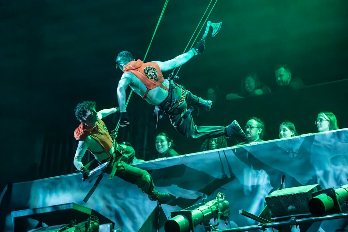 The cast performs on the theatrical arena set