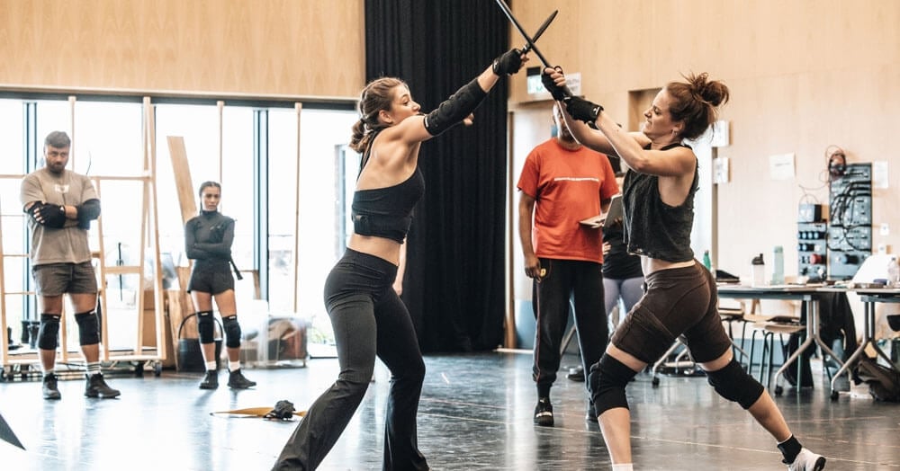 Two performers practising a staged archery sequence in rehearsal