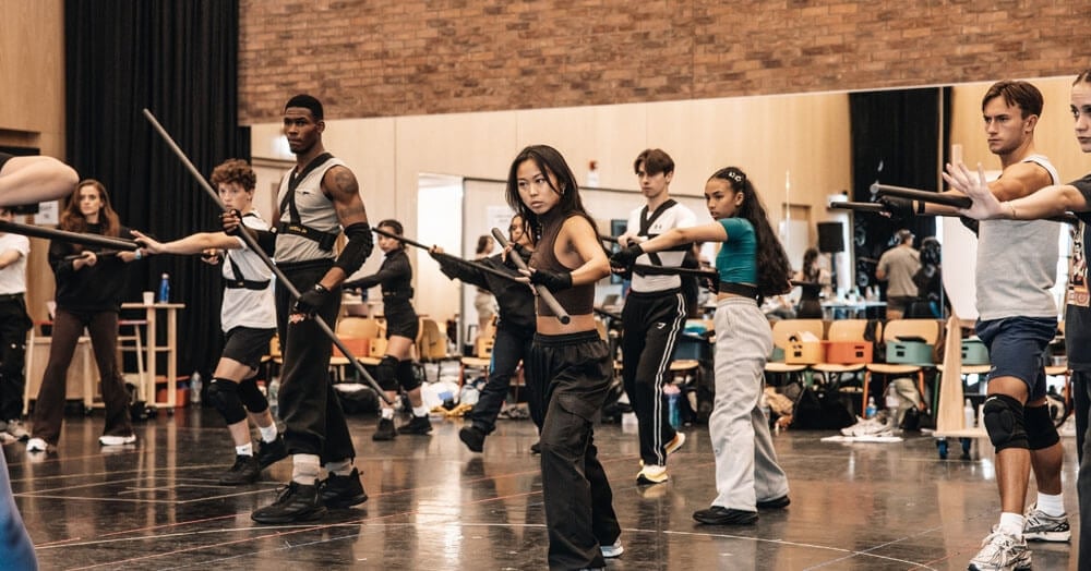 An ensemble of performers practising with bows in a rehearsal room