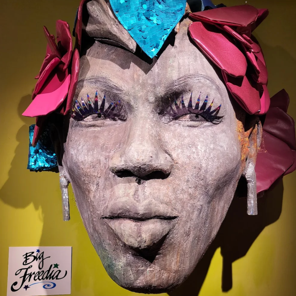Big Freedia bust with floral headband on a yellow wall at JAMNOLA