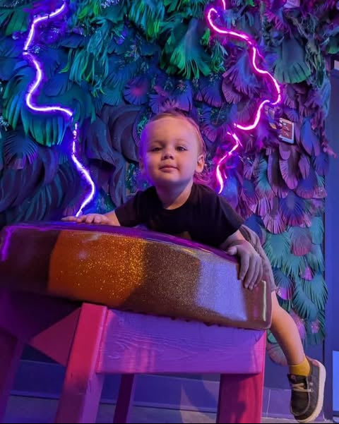 Child sitting among neon lights and foliage in a JAMNOLA exhibit