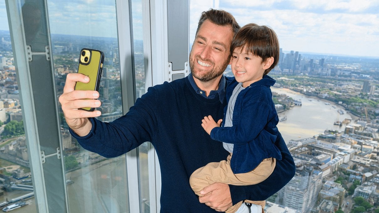 A father and child taking a selfie with the London skyline from The Shard